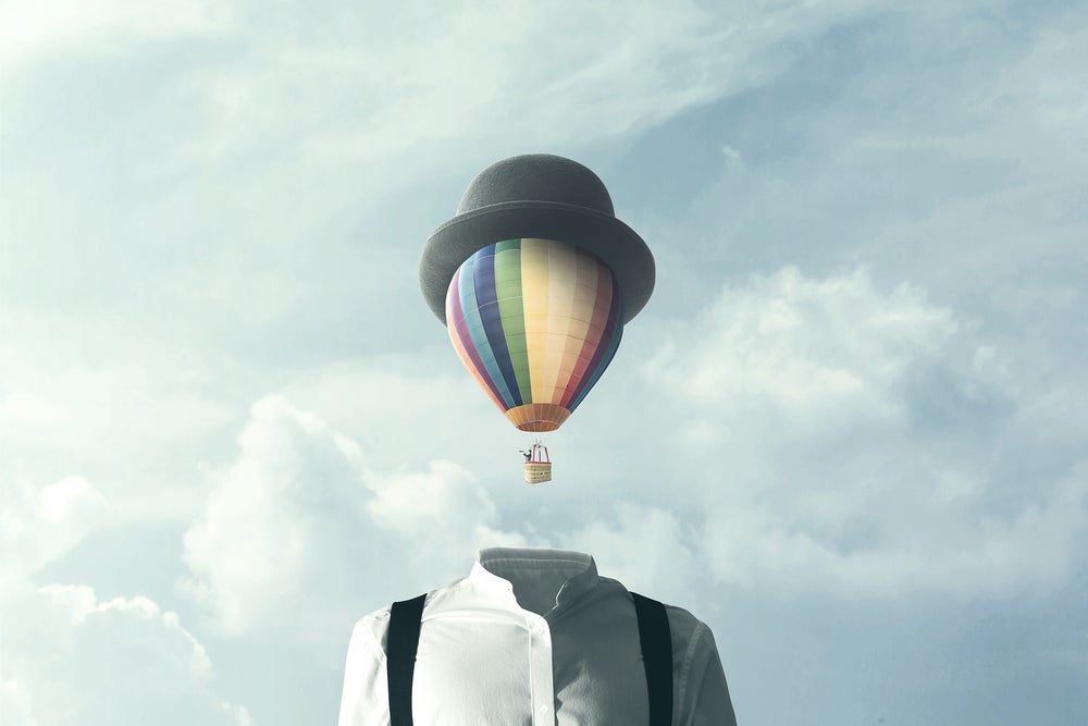 mulit-color hot air balloon and basket taking off with gray hat across its top and as though it disconnected from body below of white-and-black clothing