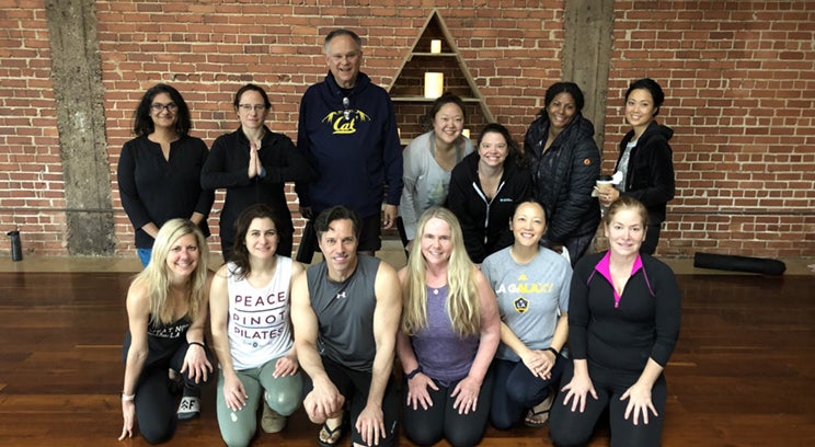 a group of a dozen people in a yoga studio smiling for the camera