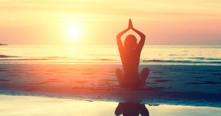 Silhouette of woman doing yoga on the beach during sunrise.