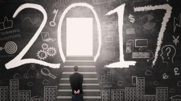 man standing at the base of stairs leading into the zero of 2017 written across a chalkboard with symbols such as a computer, money sign, gears, etc.