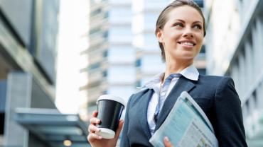 smiling female professional in a city holding a coffee cup and work documents