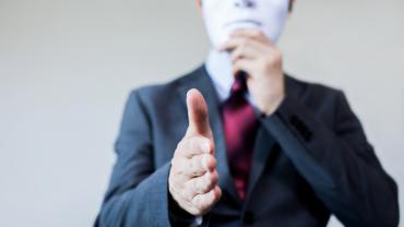 a business person with their hand held out to shake also holds a mask over their face, concealing their identity