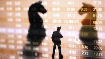 Silhouettes of two horse chess pieces and a businessman in front of stock market number on screen display