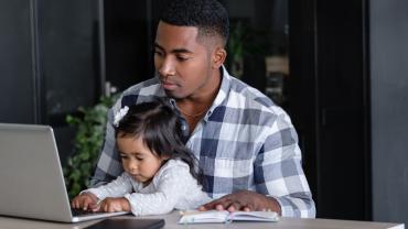 African American man working at home office with his toddler on his lap.