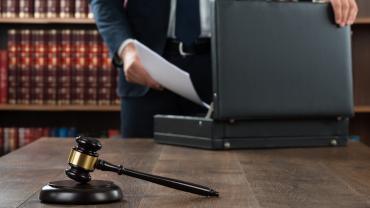 a person in a suit putting papers in a briefcase. a gavel is in the foreground